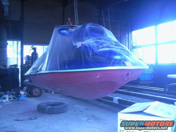 Red and blue boat covered in plastic sheeting, suspended by chains in a workshop